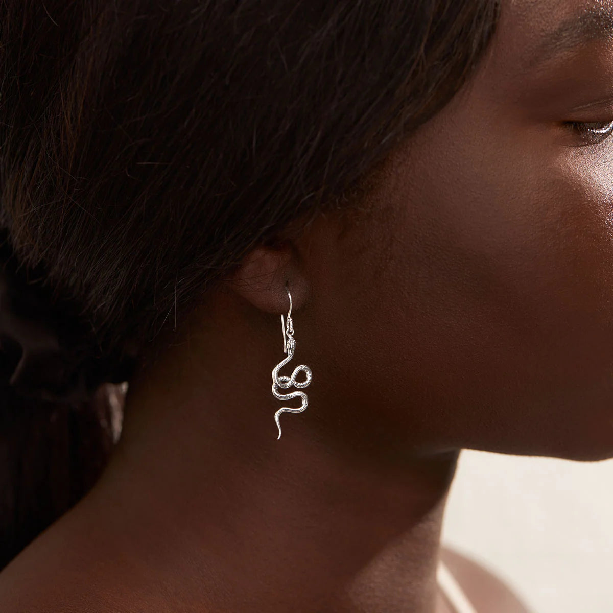 Silver snake-shaped earring worn by a person with a blurred background