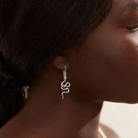 Silver snake-shaped earring worn by a person with a blurred background