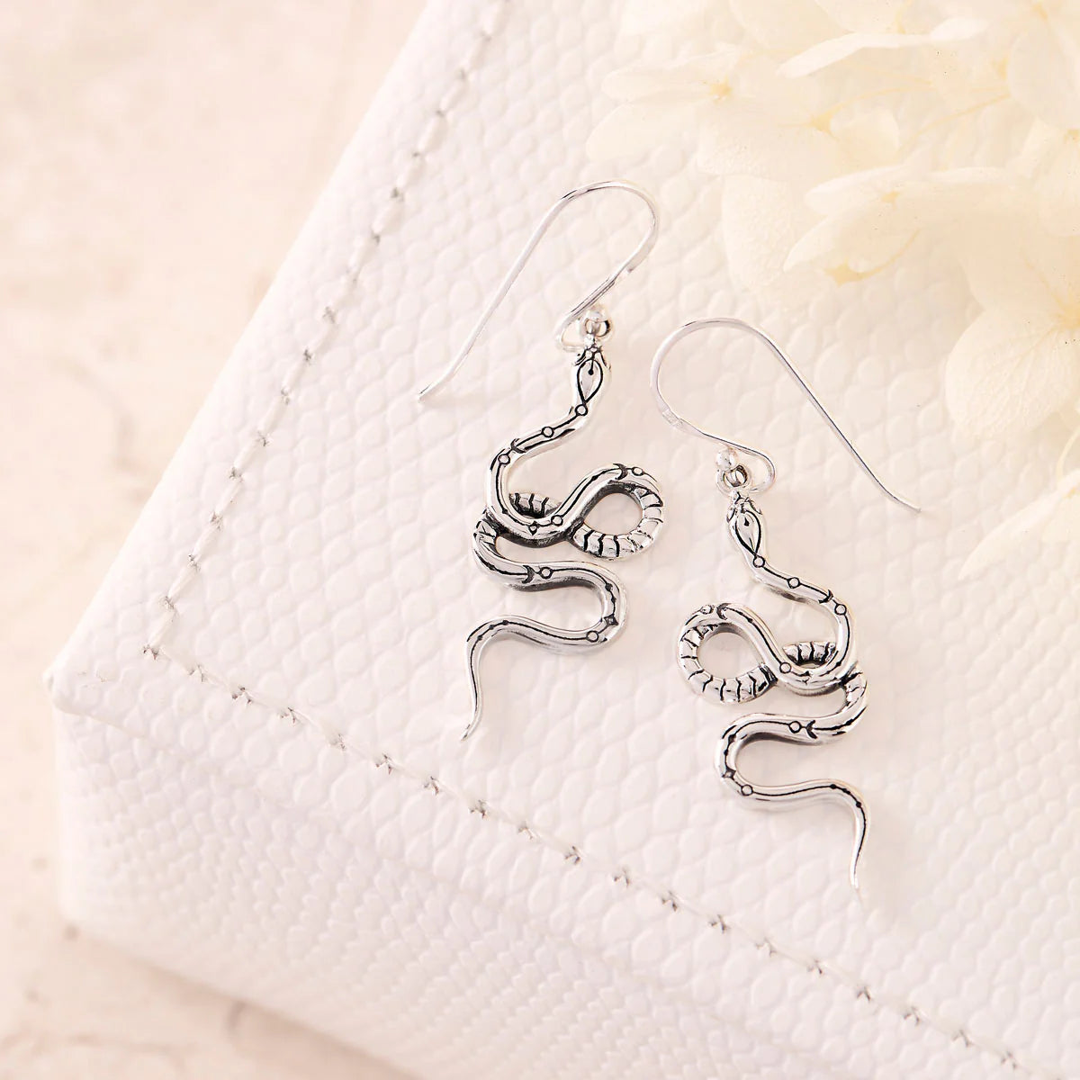 Silver snake-shaped earrings on a textured white surface