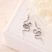 Silver snake-shaped earrings on a textured white surface
