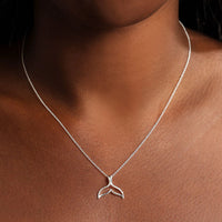 Silver necklace with a whale tail pendant on a person's neck against a dark background