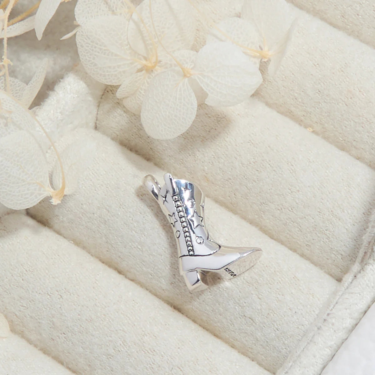Silver cowgirl boot charm on a white fabric background with flowers