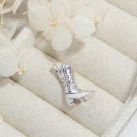 Silver cowgirl boot charm on a white fabric background with flowers