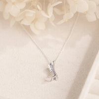 Silver necklace with a cowgirl boot  pendant on a soft beige background with flowers