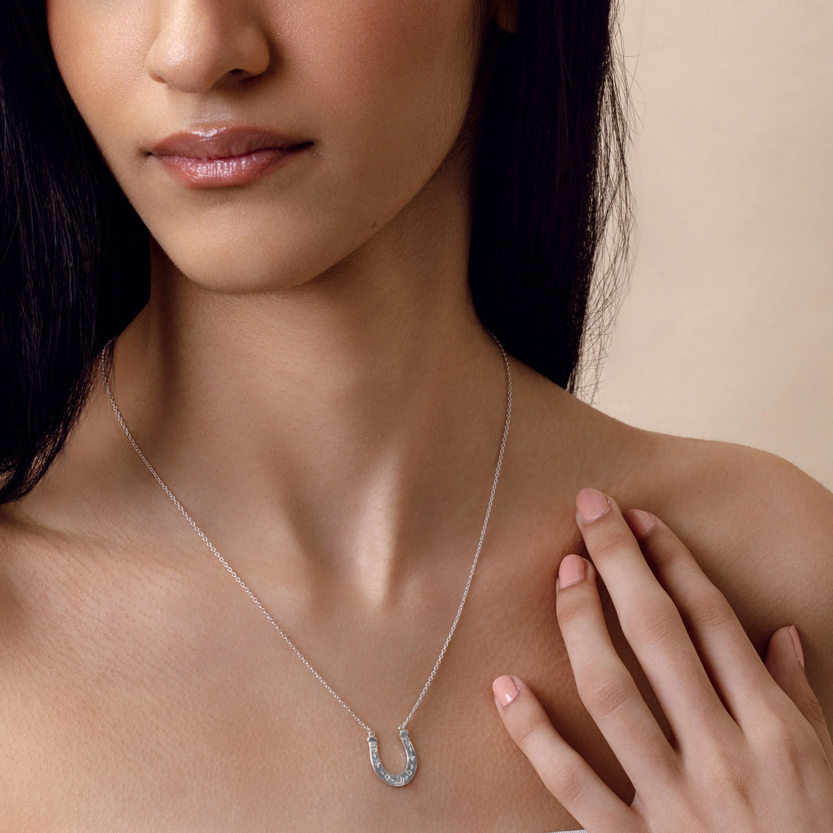 Woman wearing a silver necklace with a horseshoe pendant on a beige background