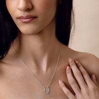 Woman wearing a silver necklace with a horseshoe pendant on a beige background