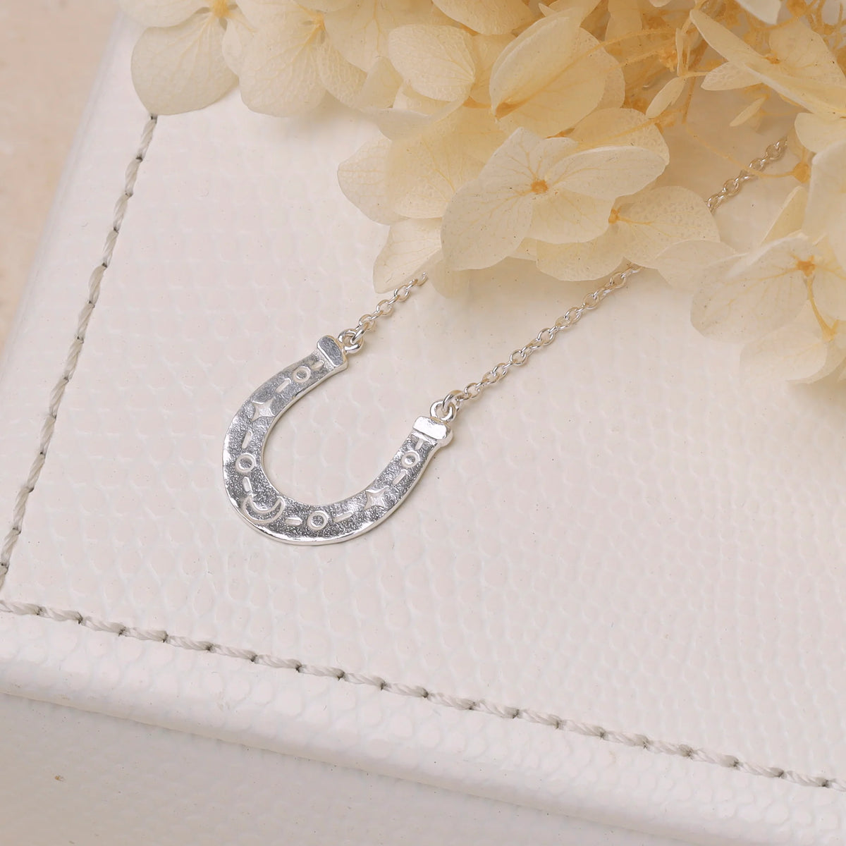 Silver horseshoe necklace on a white surface with flowers in the background