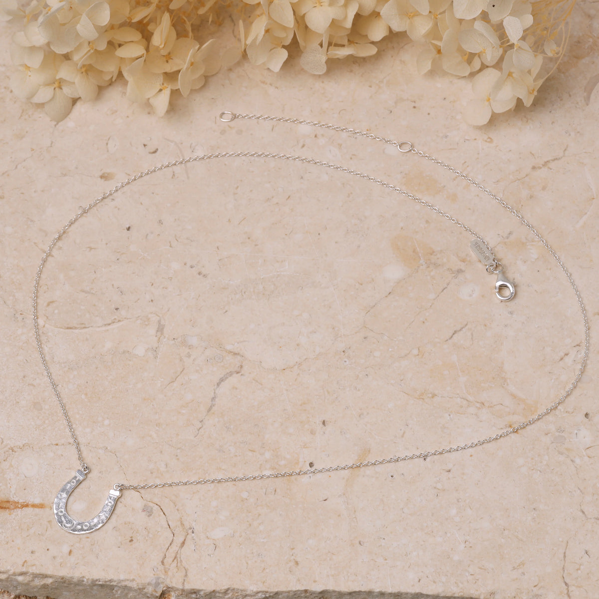 Silver necklace with a horseshoe pendant on a stone surface with flowers in the background