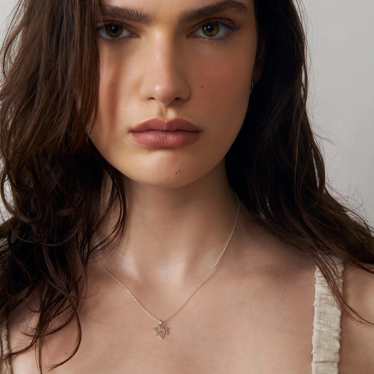 Woman wearing a delicate necklace with a small lotus-shped pendant against a neutral background