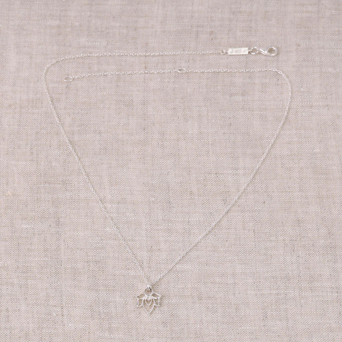 Silver necklace with a small lotus-shaped pendant on a beige fabric background