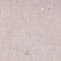 Silver necklace with a small lotus-shaped pendant on a beige fabric background