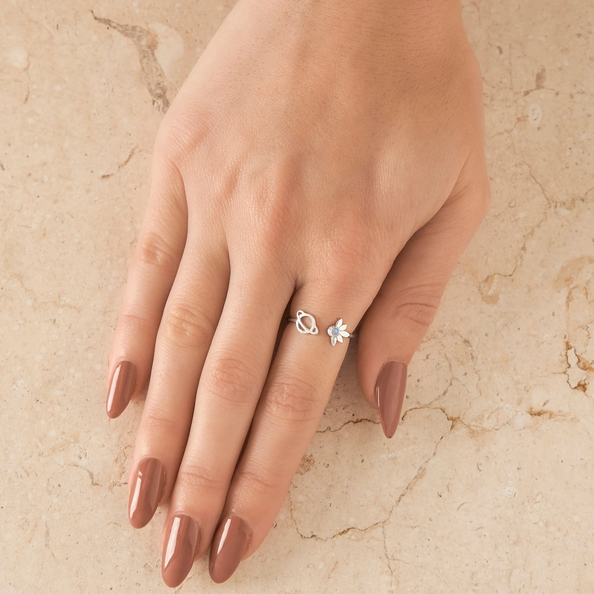 Hand wearing a silver ring with a satelite and planet design on a beige marble background