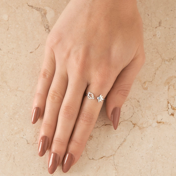 Hand wearing a silver ring with a satelite and planet design on a beige marble background