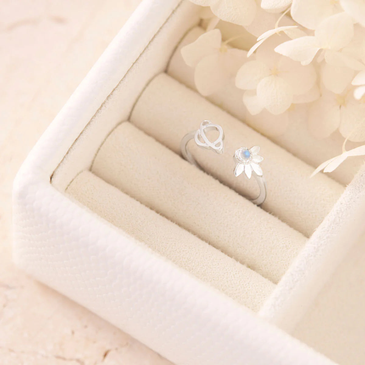 Two silver rings with satelite and planet  designsin a beige jewelry box.