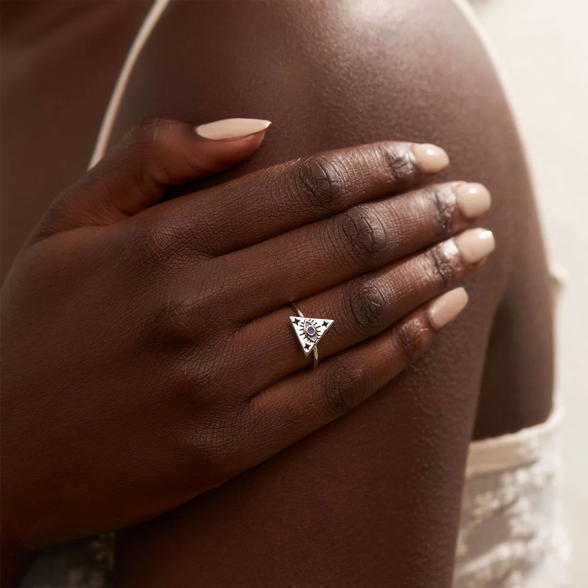 Hand wearing a silver ring with a triangle design on a blurred background