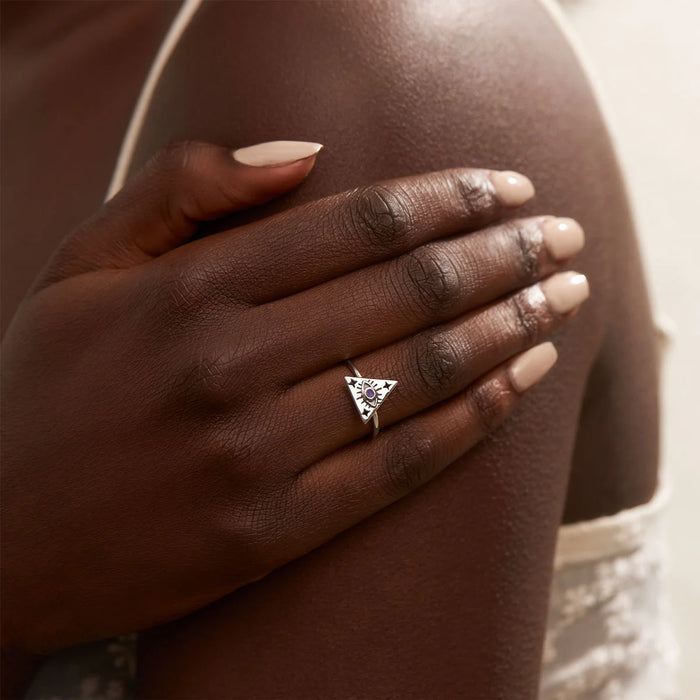 Hand wearing a silver ring with a triangle design on a blurred background