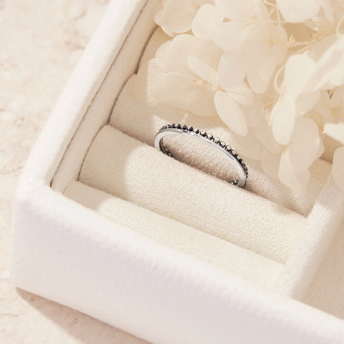 Silver ring with beaded design in a jewelry box with white flowers