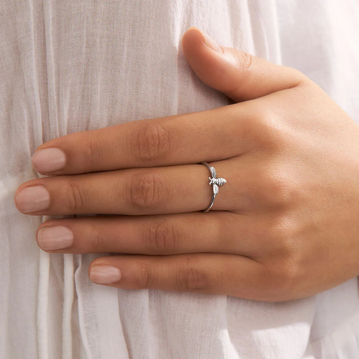 Hand wearing a silver ring with a delicate bee design against a light fabric background