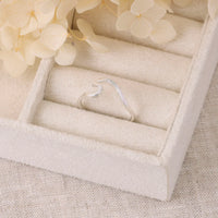 Silver wave-shaped ring in a jewelry box with beige flowers on a textured surface