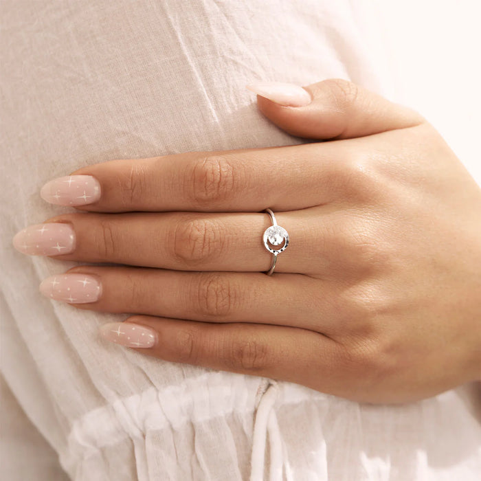 Close-up of a hand wearing a silver ring with a circular cresent moon cutout on a light background