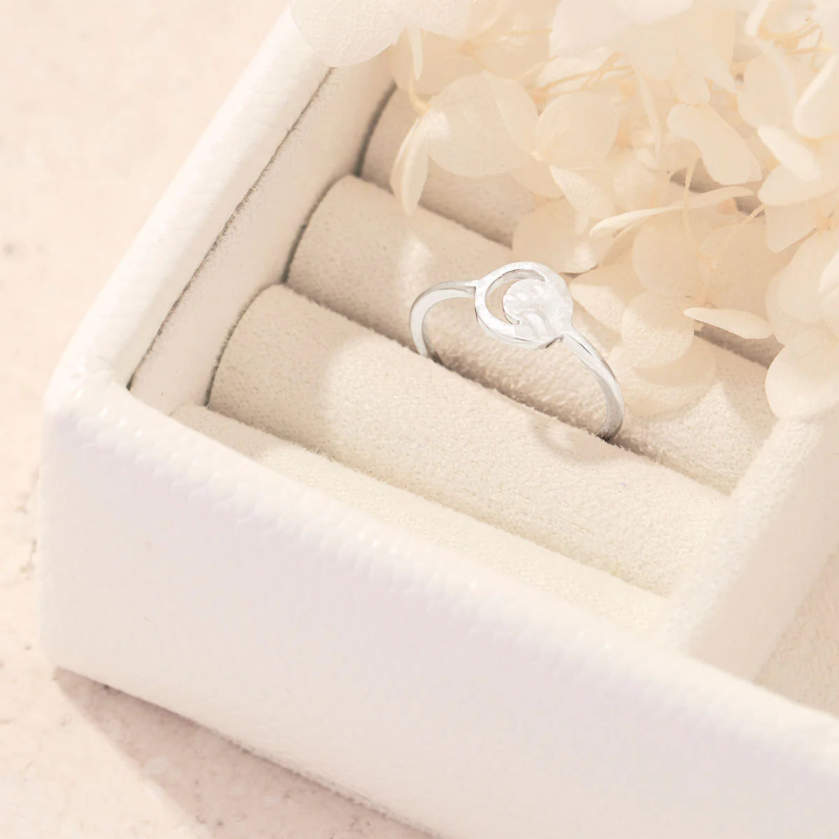 Silver ring with a circular cresent moon cutout design in a white jewelry box