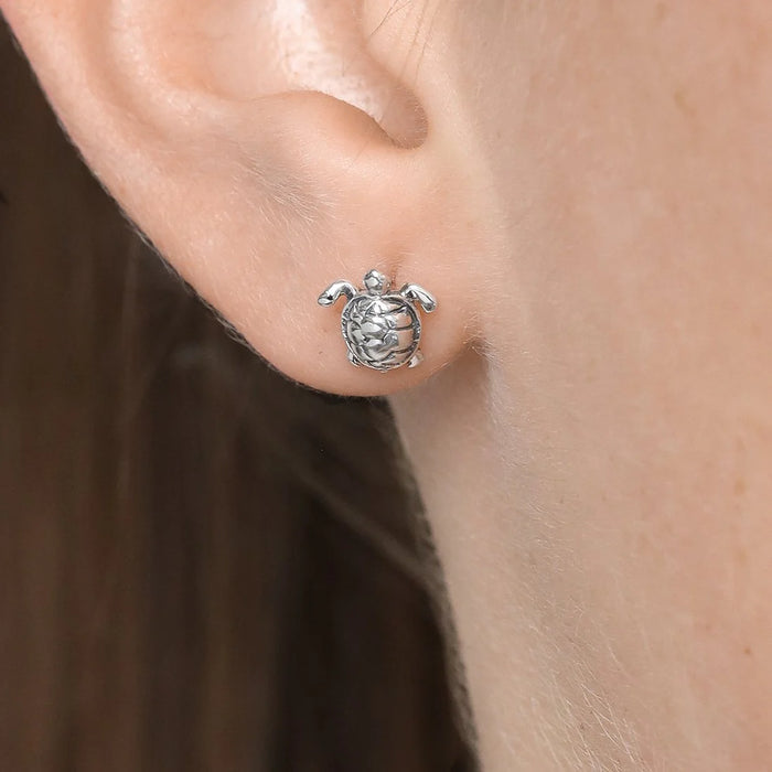 Silver turtle earring worn on a person's ear with a neutral background