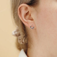 Close-up of an ear wearing a small silver earring with a circular rising sun design on a beige background.