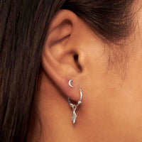 Silver hoop earring with a small cresent moon shaped stud worn by a person.
