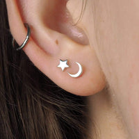 Silver star and moon earring on an ear with dark hair.