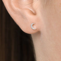 Silver crescent moon earring on a person's ear with a neutral background
