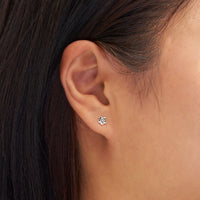 Close-up of an ear wearing a silver flower-shaped earring with dark hair.
