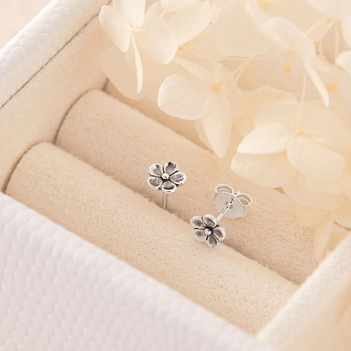 Silver flower-shaped earrings on a soft beige fabric background