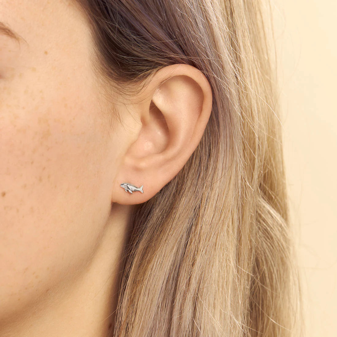 Close-up of an ear wearing a small silver whale earring.