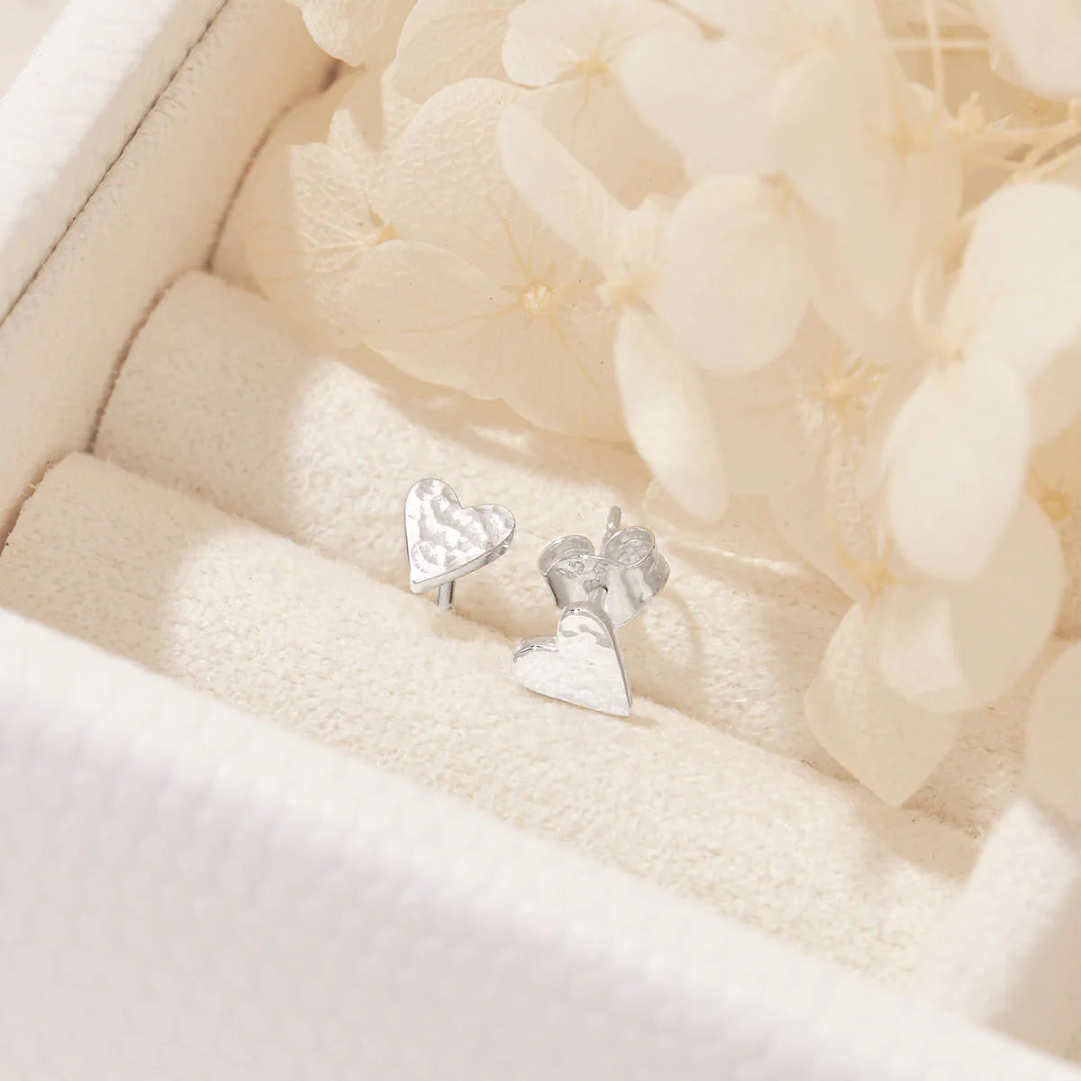 Silver heart-shaped earrings on a soft beige fabric background