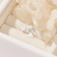 Silver heart-shaped earrings on a soft beige fabric background